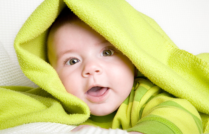 Baby mit einer grünen Decke auf dem Kopf lächelt in die Kamera